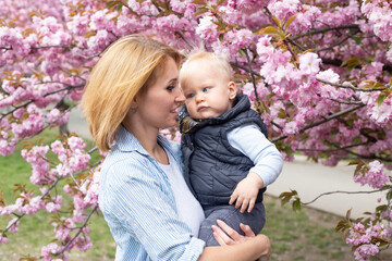 young mother with little son in her hands in park with Sakura Cherry blossom tree. Happy mother and child.