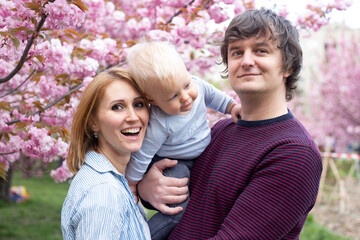 Portrait of hipster parents with their son in the spring near the Japanese cherry sakura meet spring. Sakura very beautifully blooms with pink flowers