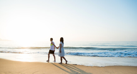 Young couple holding hand walking on beach.