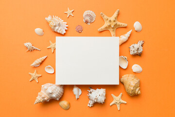 Summer time concept with blank greeting card and blank white paper on colored background. Seashells from ocean shore in the shape of frame separated with space for text top view