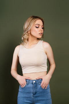 young woman in beige top posing with hands in pockets of jeans isolated on green.