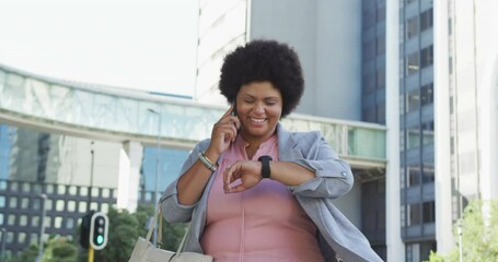 Happy plus size biracial woman checking smartwatch and walking in city