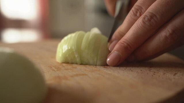 A woman cuts an onion on a wooden board.
