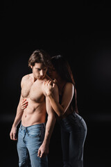 Young woman in jeans touching sexy boyfriend isolated on black.