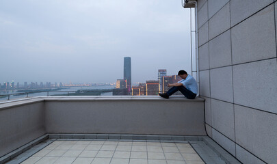 Depressed man sitting on the rooftop railing