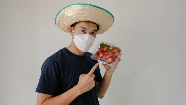 Man wearing a mask holding a box of strawberries. Please Mot. Strawberry fruit souvenirs.
