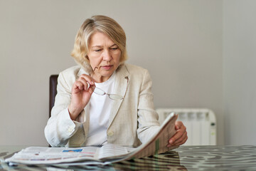 senior woman reading newspaper at home