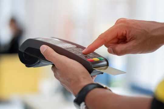 Cashier holding credit card reader machine on hand with insert card for payment process from customer, pressing the value number or price of products to charge the online payout, online deduction