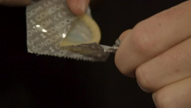 Hands opening condom package and revealing new condom