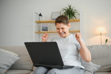 Excited mature woman looking at laptop screen, reading good news in message, celebrating online lottery win, rejoicing success, overjoyed older female sitting on couch at home, using computer.