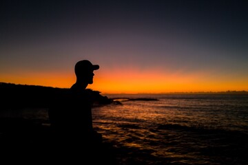 Fototapeta na wymiar Sillhouette of man wearing baseball cap looking out to the ocean at sunrise