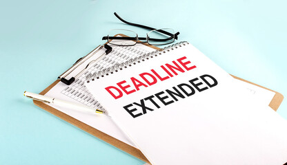 DEADLINE EXTENDED text on notepad on clipboard with chart on blue background, concept closeup. Business and finance concept