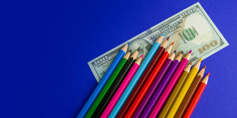 multicolored pencils on souvenir dollar bills. items lie on a blue background. Banner for insertion...
