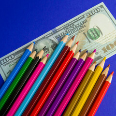 multicolored pencils on souvenir dollar bills. items lie on a blue background. Square image.