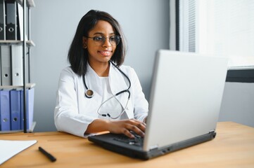 Fototapeta na wymiar healthcare, medical and technology concept - african female doctor with laptop