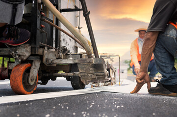 A road worker paints and observes pedestrian lines crossing the road on asphalt surface using a paint truck during a sidewalk maintenance work on the Asian Highway.