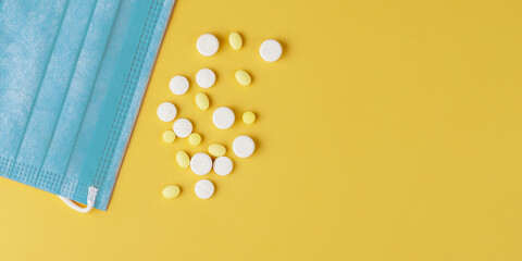 Blue face mask, white and yellow tablets on yellow background with copy space.  health care concept.