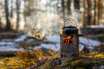 Burning wood stove with boiling kettle in the forest close-up, object in focus, the background is blurred.