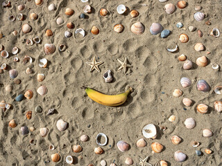 Funny face made of seashell, starfish and banana on beach sand