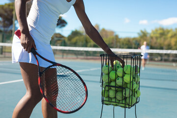 Midsection of female african american player practicing tennis at court on sunny day