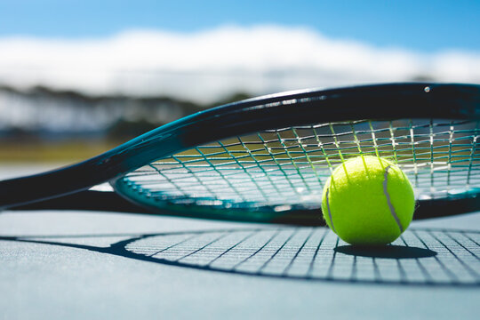 Close-up of green tennis ball with racket at court on sunny day