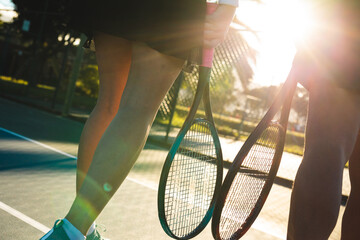 Back lit young female biracial tennis players walking with rackets at court