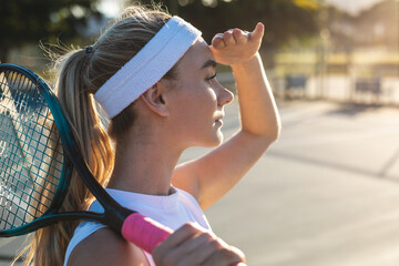 Naklejka premium Side view of young caucasian female tennis player shielding eyes while looking away with racket