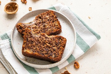 Pieces of american homemade sliced banana bread with chopped walnuts, chocolate and cinnamon on light background. Breakfast concept with milk. Vegan healthy food. Selective focus.