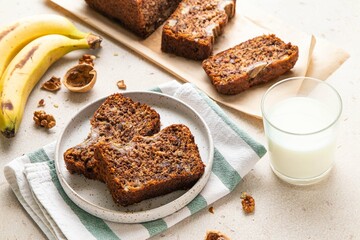 Pieces of american homemade sliced banana bread with chopped walnuts, chocolate and cinnamon on light background. Breakfast concept with milk. Vegan healthy food. Selective focus.