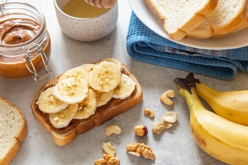Toast with tasty nut butter and banana slices on light background. Walnut, hazelnut and cashew nut spread in glass jar. Homemade breakfast sandwich. Healthy food concept.