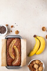 Traditional American homemade banana bread with chopped walnuts, chocolate and cinnamon in loaf pan on light background. Fruit cake. Healthy vegan desserts concept. Top view, copy space.