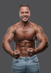 Fototapeta premium Studio shot of handsome guy with muscular build dressed in jeans posing against grey background.