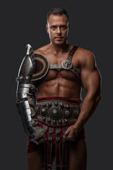 Fototapeta na wymiar Shot of brutal roman gladiator dressed in light armor staring at camera against gray background.