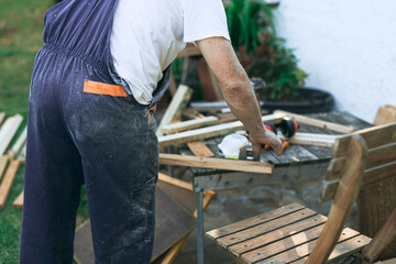 man in dungarees with his back turned cutting wood