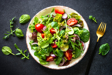 Green salad. Fresh salad leaves and vegetables in white plate at black table. Top view image with copy space.