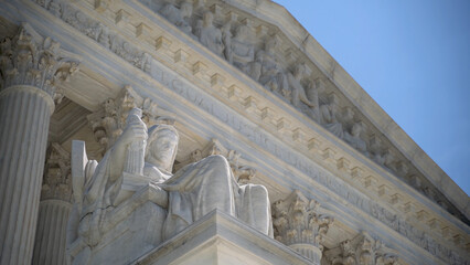 Closeup of sculpture on the Supreme Court building of The Three Fates with Equal Justice slightly out of focus in the distance.