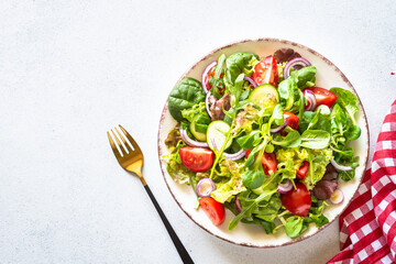 Green salad, veggie dish. Fresh salad leaves and vegetables in white plate. Healthy vegan food, diet food. Top view image.