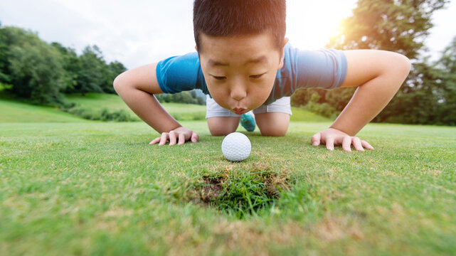 Little boy blowing golf ball into hole