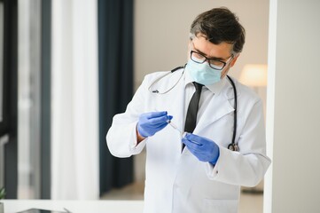 Male doctor wearing uniform, mask, medical gloves holding syringe taking covid 19 corona virus vaccine from vial bottle preparing for injection. Coronavirus immunization flu treatment vaccination.