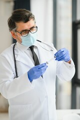 Mid aged male doctor wearing protective mask holding a syringe with vaccine.