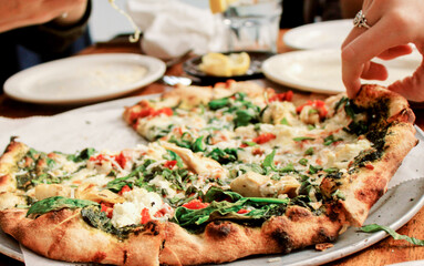 Sliced pieces of spinach greek style pizzas at a restaurant table gathered around by a group of...