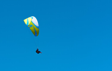 Paragliding pilot gliding down from high in blue sky background