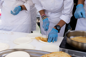 Three unrecognizable chefs cuting and preparing crepes at a profession fair. Handmade cooking