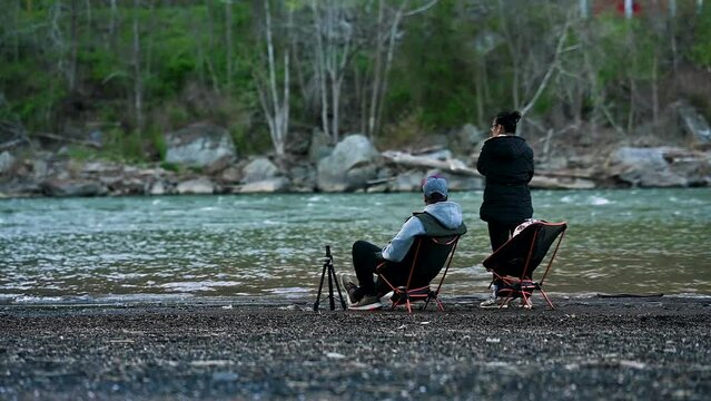 Asian Couple On Chairs At Riverside Camp Site At New River Gorge Forest, United States