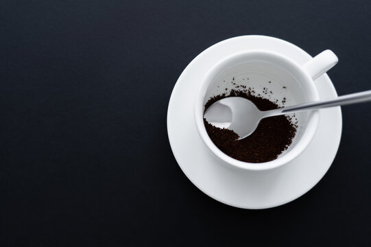 top view of ground coffee in cup with spoon on black.