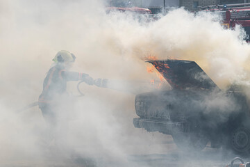 A firefighter extinguishes a car with a fire extinguisher. Fire extinguisher extinguishes a burning...