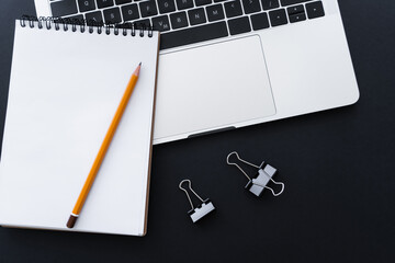 top view of fold back clips near pencil on notebook and laptop on black.