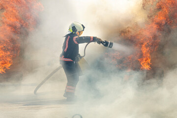 The hero firefighter stands among the smoke and fire and extinguishes the fire with a stream of...