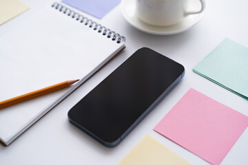 close up of stationery near smartphone with blank screen on white.