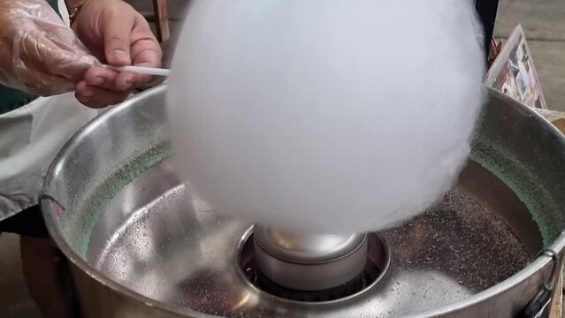 A man's hand is spinning a cotton candy machine for children during the holidays.